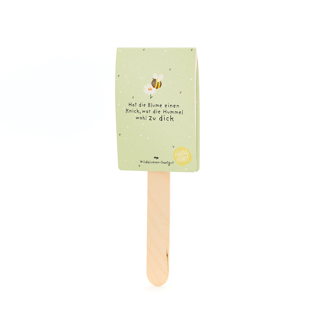 Etiqueta de papel verde con motivo de abeja y la frase “Si la flor tiene una torcedura, el abejorro probablemente estaba demasiado gordo” en un palo de madera.