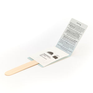 Un palo de madera con un paquete abierto que contiene una bolsa de semillas e instrucciones impresas en alemán.