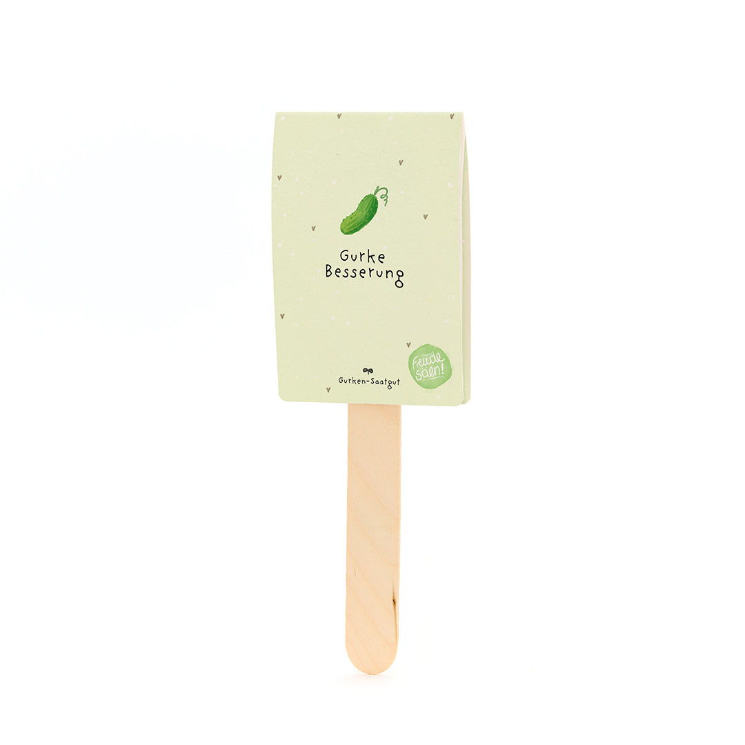 Un palo de madera con una etiqueta de papel de color verde beige que representa un pepino dibujado y el texto "Mejora del pepino".