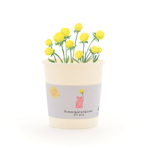 Taza con flores de gomita de color amarillo y una etiqueta que dice “Flor de gomita de osito para ti”.