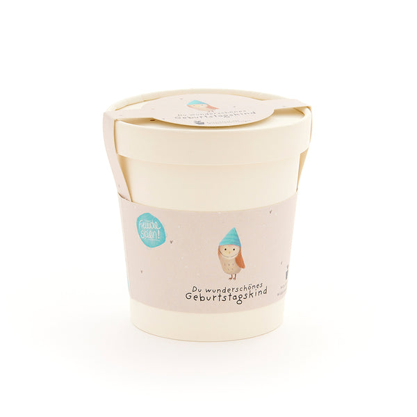 Taza beige con tapa y etiqueta que representa un búho con sombrero azul y la inscripción “Hermoso cumpleañero”.