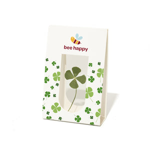 Bolsa de papel con un trébol de cuatro hojas y el texto "bee happy", así como una ilustración de una abeja.
