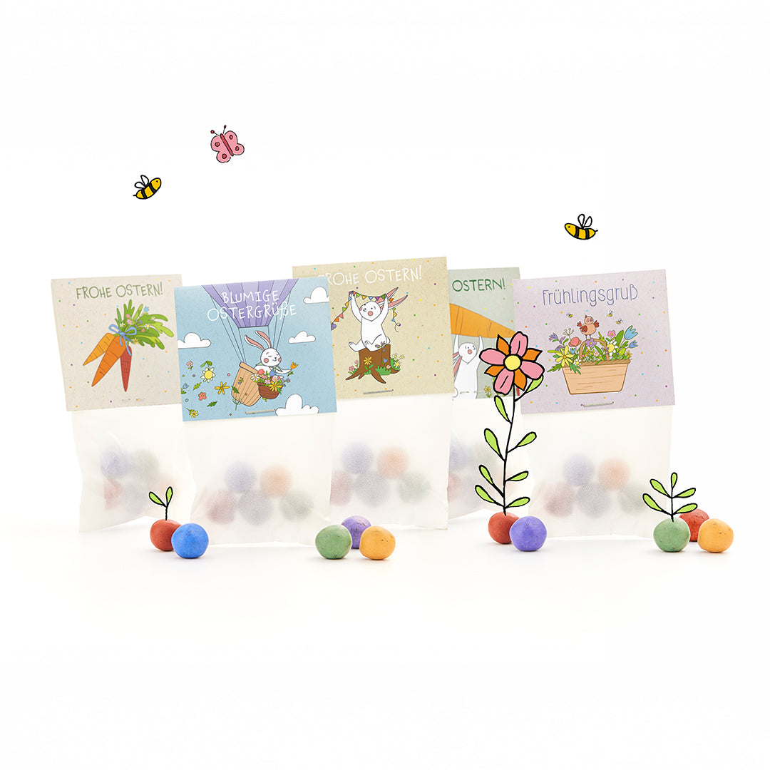 Cuatro bolsas de Pascua con bolas de colores, cada una con alegres motivos ilustrados de Pascua y primavera y saludos en alemán como "Felices Pascuas" y "Saludos de primavera", rodeadas de flores, abejas y mariposas dibujadas.