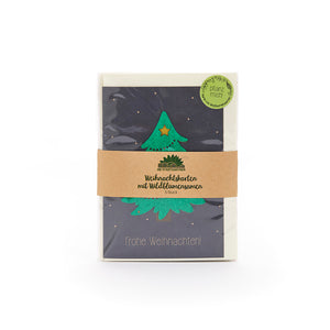 Tarjeta de Navidad con un árbol de Navidad verde y una estrella, en un paquete con una cinta de papel marrón y la inscripción "Tarjetas de Navidad con semillas de flores silvestres", al lado una pegatina verde con "Plántame".