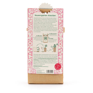 Parte posterior de una bolsa de semillas de flores, descripción e instrucciones en alemán, diseño floral rosa, un logo rojo del Seed Festival en la parte inferior.