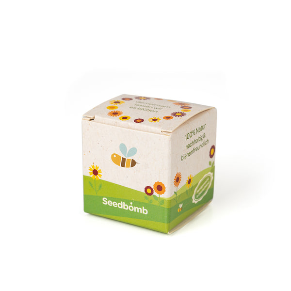 Pequeña caja etiquetada como “Seedbomb” rodeada de ilustraciones florales, con referencias a ser 100% natural y amigable con las abejas.