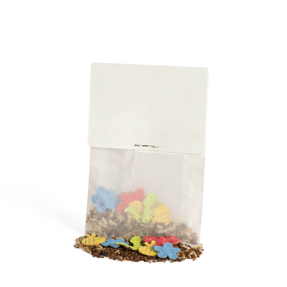 Pequeña bolsa de papel con galletas de colores con forma de flores y animales, algunas de las cuales se han caído, sobre un fondo blanco.
