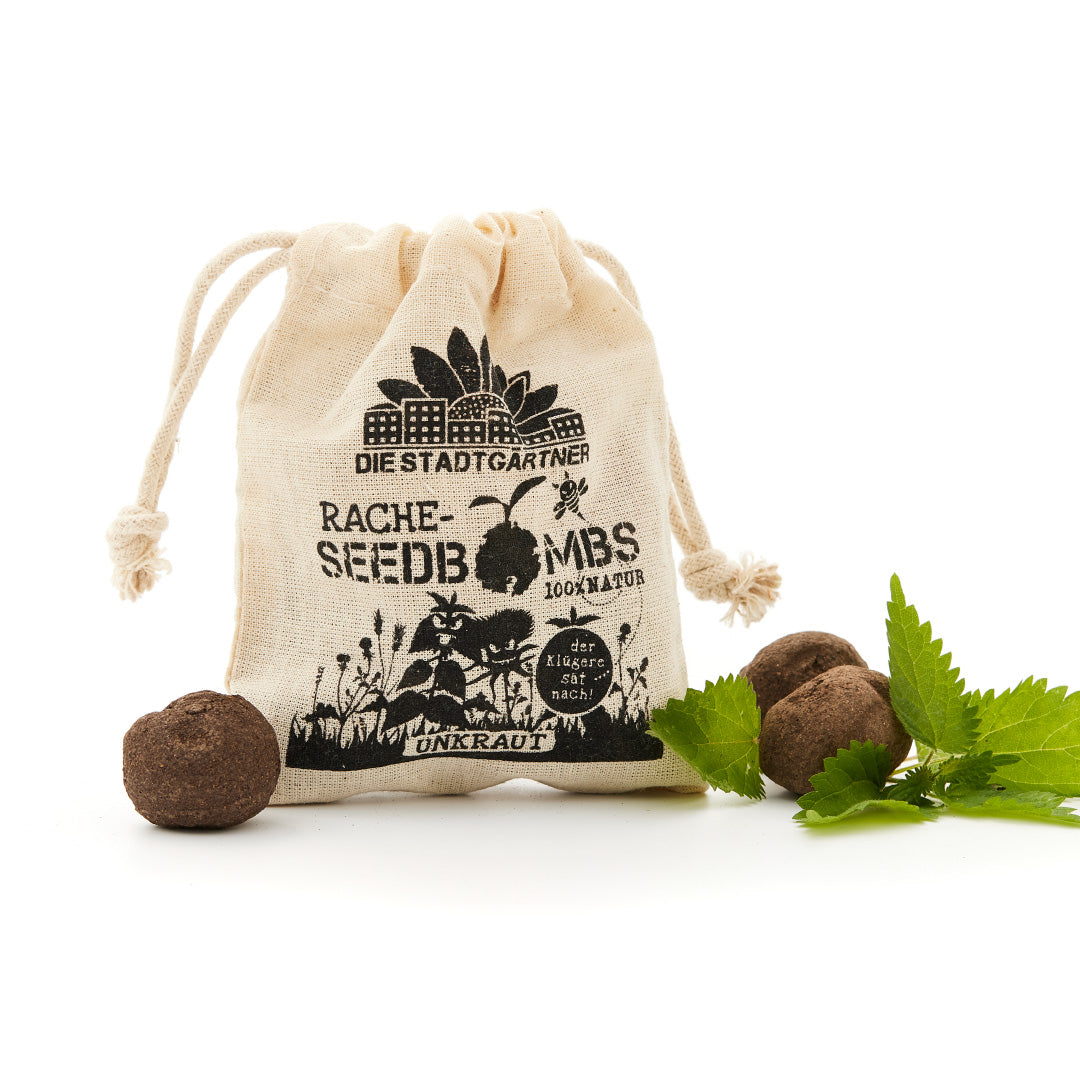 "Una pequeña bolsa de yute con el estampado 'LA VENGANZA DEL JARDINERO DE LA CIUDAD BOMBAS DE SEMILLAS 100% NATURALES' y algunas bombas de semillas junto a hojas verdes frescas sobre un fondo blanco".