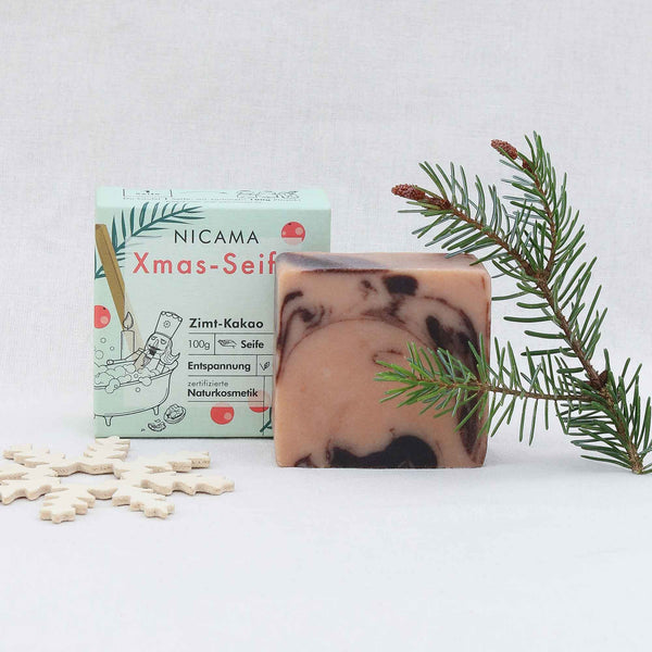 Jabón artesanal con aroma a canela y cacao junto a su packaging y decoración navideña.