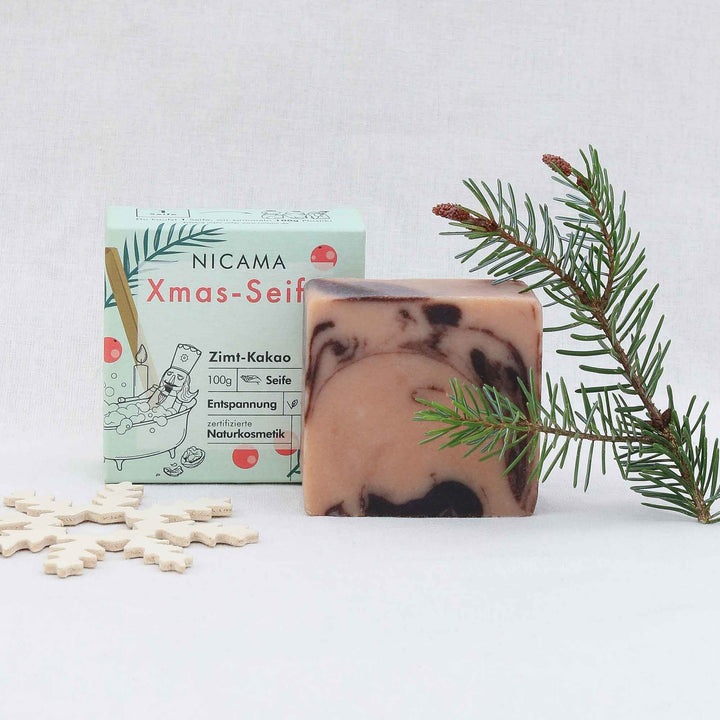 Jabón artesanal con aroma a canela y cacao junto a su packaging y decoración navideña.