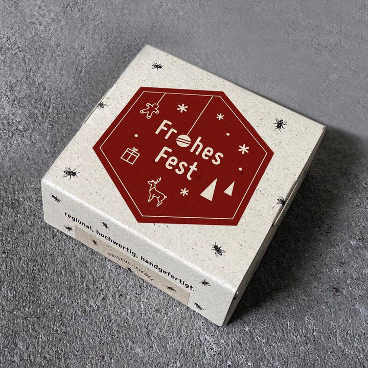 Caja de regalo con la inscripción "Feliz Navidad" y símbolos navideños sobre fondo gris.