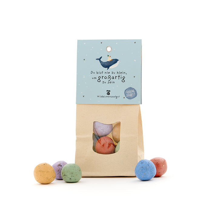 Bolsa de papel con bombas de semillas de colores, etiqueta con una ballena y el dicho "Nunca eres demasiado pequeño para ser grande".