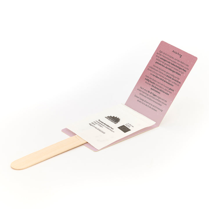 Un kit de cultivo con un palo de madera, un paquete de semillas e instrucciones desplegadas en alemán.