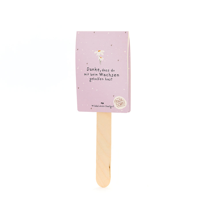 Palo de madera con tarjeta morada que dice "Gracias por ayudarme a crecer" y "Semillas de flores silvestres".