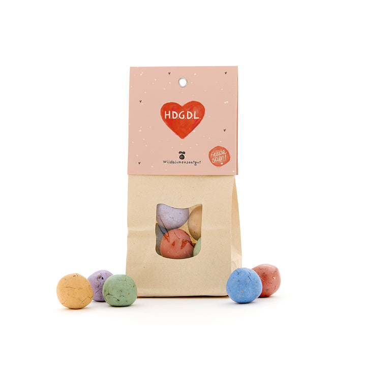 Bolsa de papel con bolas de semillas de colores, etiqueta con un corazón rojo y la inscripción "H.D.G.D.L."