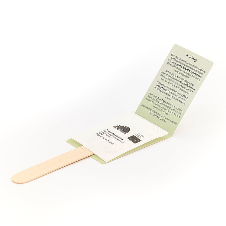 Palitos de madera con paquetes de semillas e instrucciones ilustradas en alemán.