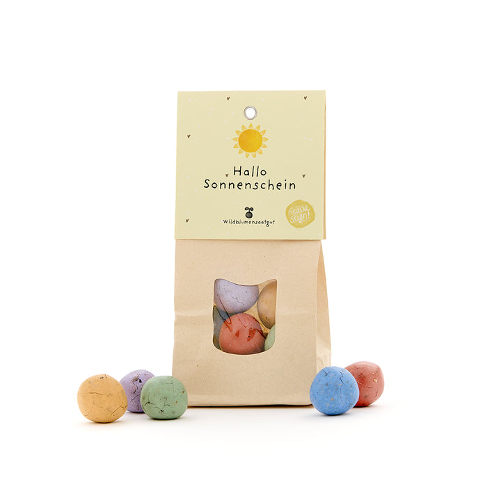 Bolsa de papel con ventana, llena de bolas de semillas de colores, etiqueta con la inscripción “Hello Sunshine”.