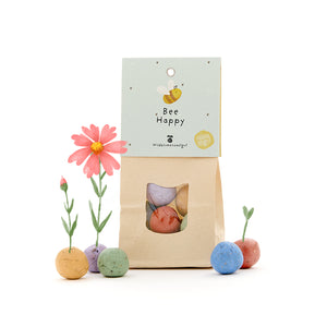 Bolsa de papel con la inscripción "Bee Happy" y coloridas bombas de semillas cultivando flores.
