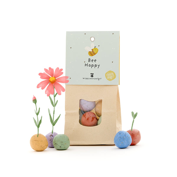 Bolsa de papel con la inscripción "Bee Happy" y coloridas bombas de semillas cultivando flores.