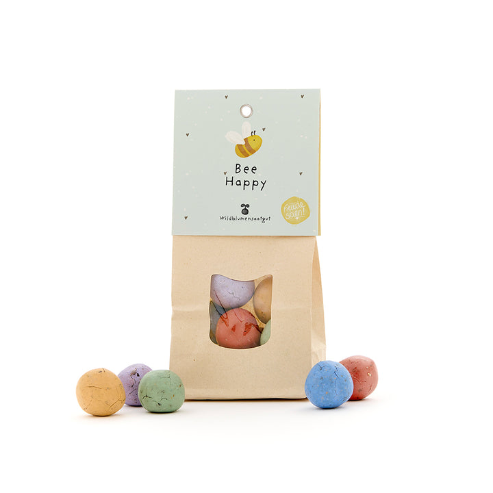 Bolsa de papel con bombas de semillas de colores y etiqueta "Bee Happy" para flores silvestres.
