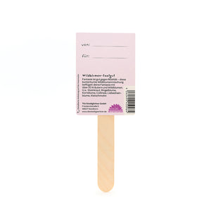 Palitos de madera con una etiqueta rosa que dice "von" y "für" y proporciona información sobre semillas de flores silvestres en alemán.
