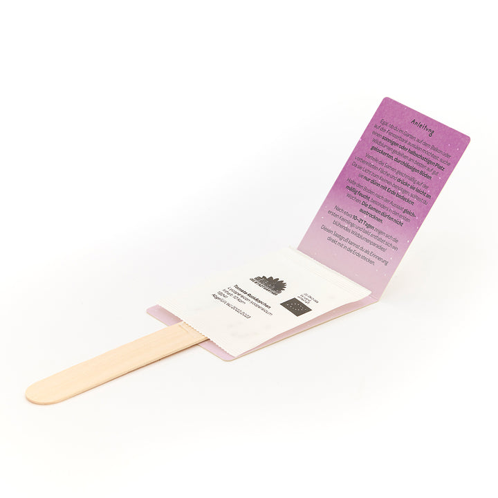 Un kit de plantación con palos de madera, paquetes de semillas e instrucciones desplegadas en cartón violeta.