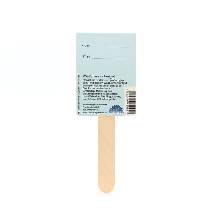 Parte posterior de una barra de semillas de flores silvestres con texto descriptivo, espacio para las entradas "de" y "para", así como información del producto y del fabricante sobre un fondo azul claro.