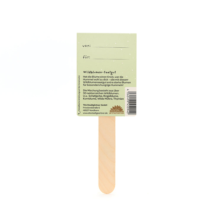 Palo de madera con una etiqueta impresa en verde que describe las semillas de flores silvestres, incluyendo "de" y "para" los campos, y brinda información sobre las especies de flores silvestres incluidas.