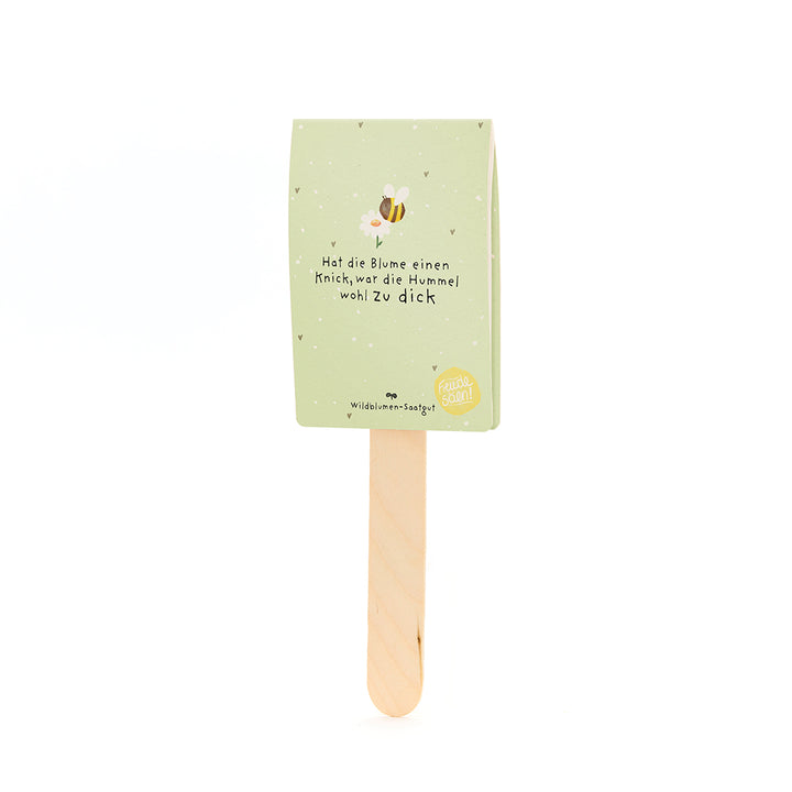 Etiqueta de papel verde con motivo de abeja y la frase “Si la flor tiene una torcedura, el abejorro probablemente estaba demasiado gordo” en un palo de madera.