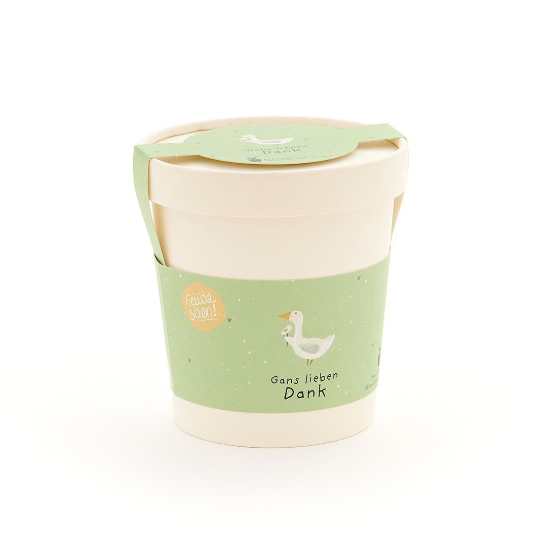 Taza beige con etiqueta verde que muestra el dibujo de un ganso y el texto “Muchas gracias, ganso”.