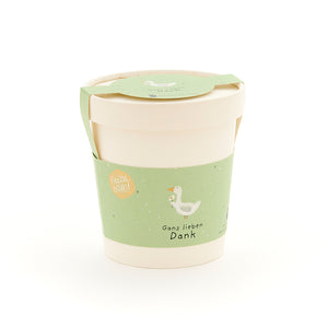 Taza beige con etiqueta verde que muestra el dibujo de un ganso y el texto “Muchas gracias, ganso”.