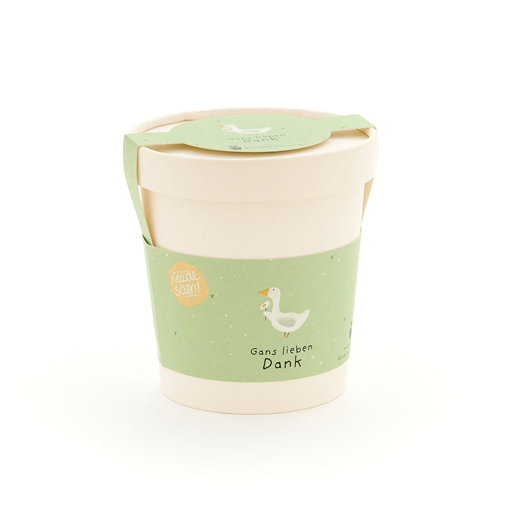Taza beige con etiqueta verde que muestra el dibujo de un ganso y el texto “Muchas gracias, ganso”.