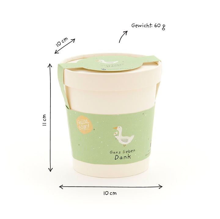 Taza con etiqueta verde, un ganso dibujado y la inscripción "Gans lieben Dank" (Muchas gracias), junto a ella las dimensiones y el peso (10 cm x 10 cm x 11 cm, 60 g).