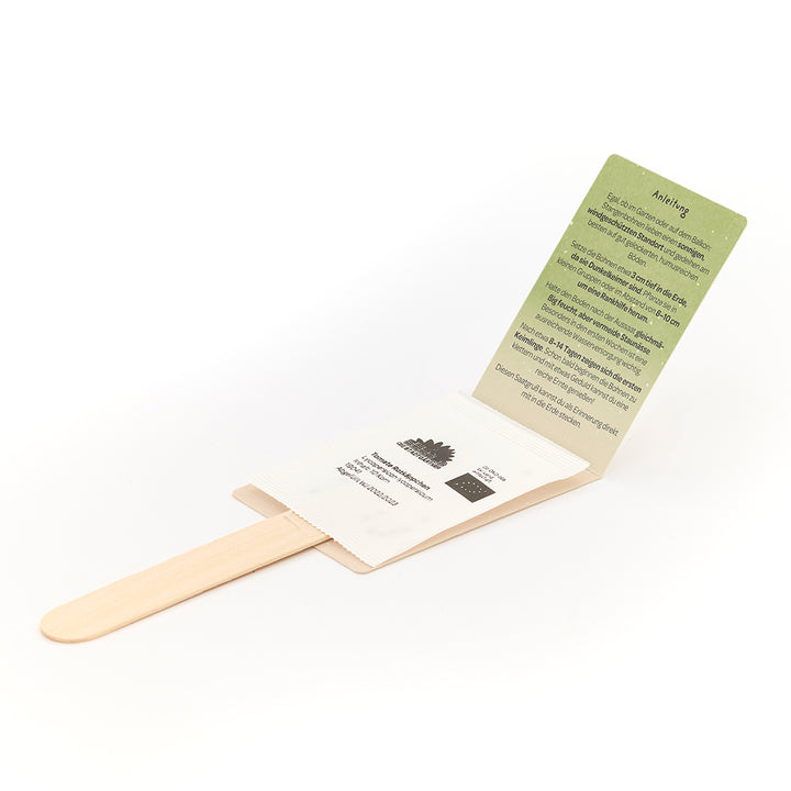 Palo de madera con un sobre que contiene una tarjeta de instrucciones verde y un sobre con semillas.
