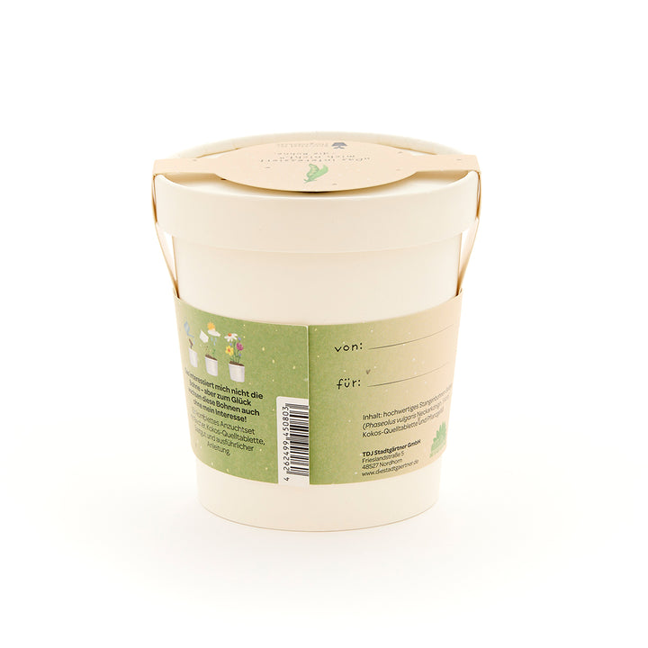 Maceta beige con etiqueta verde, campos de texto "de:" y "para:", y descripción y dibujos de plantas en la parte posterior.