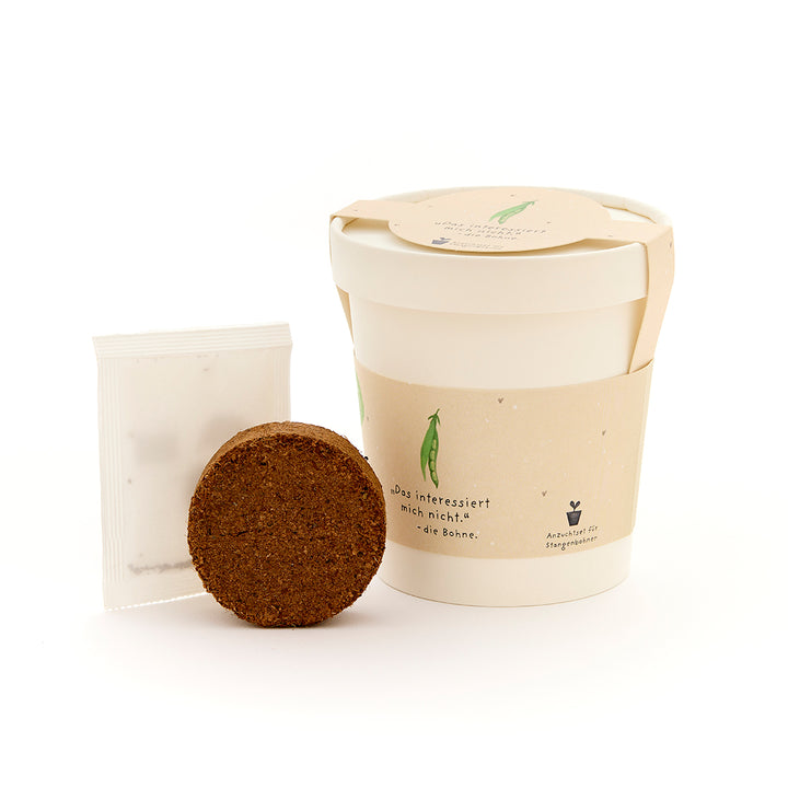 Un kit de plantación con un bloque de tierra redondo, una bolsa para semillas y un recipiente beige.