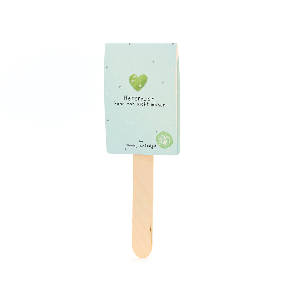 Palo de madera con un cartel de color azul claro que lleva un corazón verde y el texto "No puedes cortar un corazón que corre" y "Semillas de pasto".