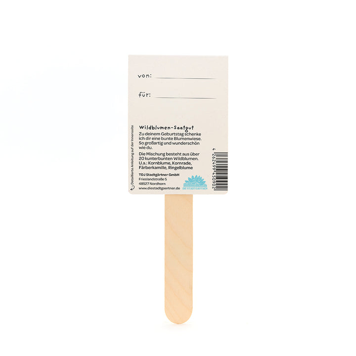 Reverso de un regalo de semillas de flores silvestres con un palo de madera, campos para "de" y "para" y una descripción de la mezcla de semillas de flores en alemán.