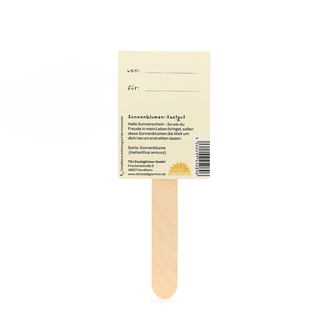 Un palo de madera con una etiqueta adherida que describe las semillas de girasol y que contiene casillas "de" y "para" para rellenar.