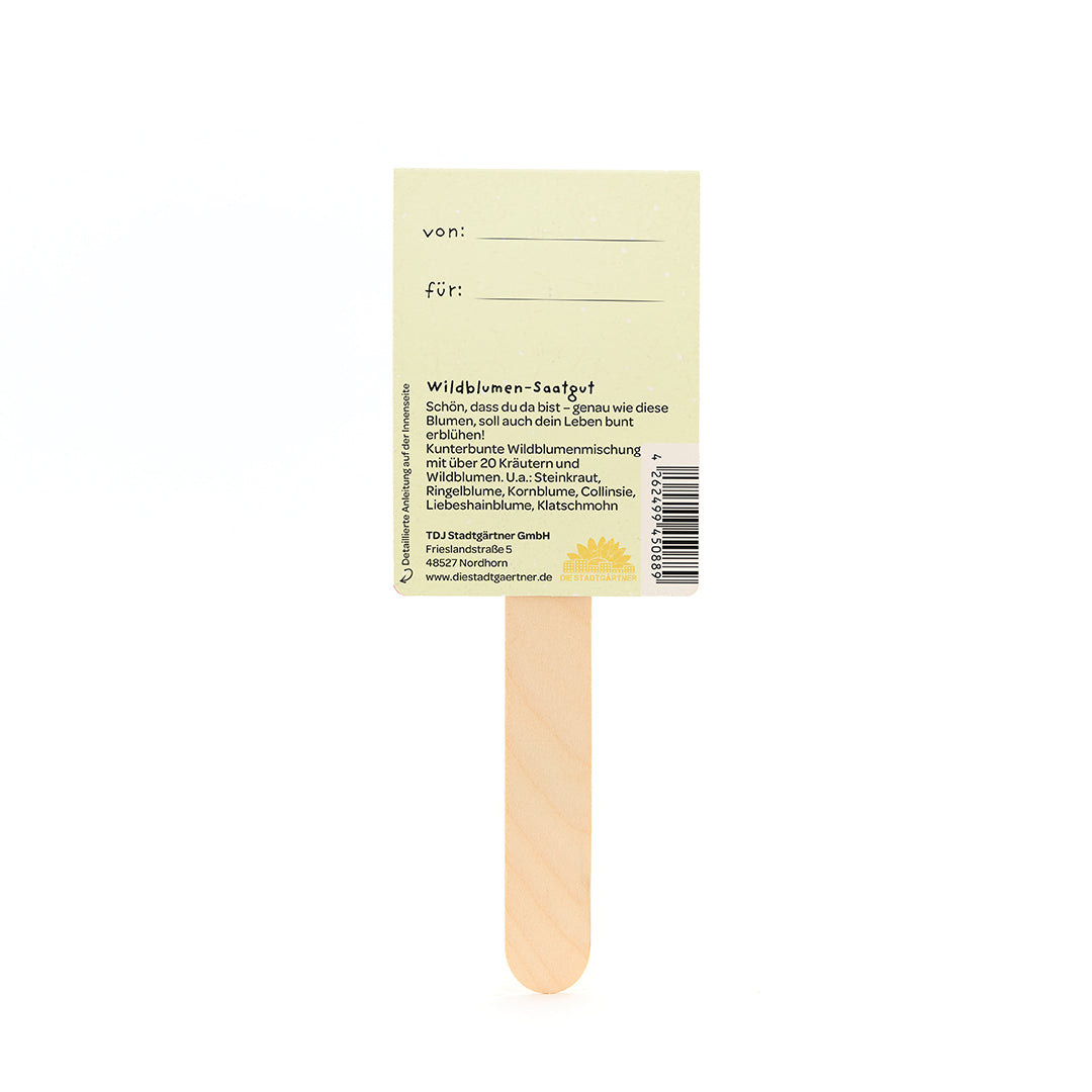 Parte posterior de un palito de semillas de flores silvestres de madera con una etiqueta amarilla y una descripción en alemán.