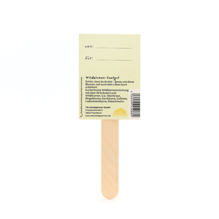 Parte posterior de un palito de semillas de flores silvestres de madera con una etiqueta amarilla y una descripción en alemán.