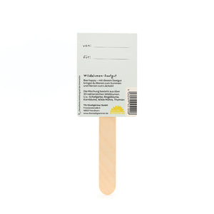 Parte posterior de un paquete de semillas con un palito de madera que contiene información sobre semillas de flores silvestres y espacio para "de:" y "para:".