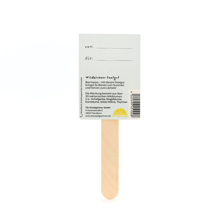 Parte posterior de un paquete de semillas con un palito de madera que contiene información sobre semillas de flores silvestres y espacio para "de:" y "para:".