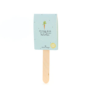 Un palo de madera con una etiqueta azul claro, un dibujo de zanahoria y el texto “Me gustas con todas tus zanahorias”.