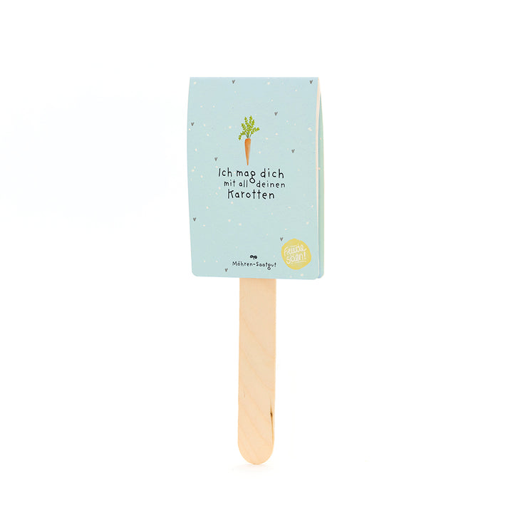 Un palo de madera con una etiqueta azul claro, un dibujo de zanahoria y el texto “Me gustas con todas tus zanahorias”.