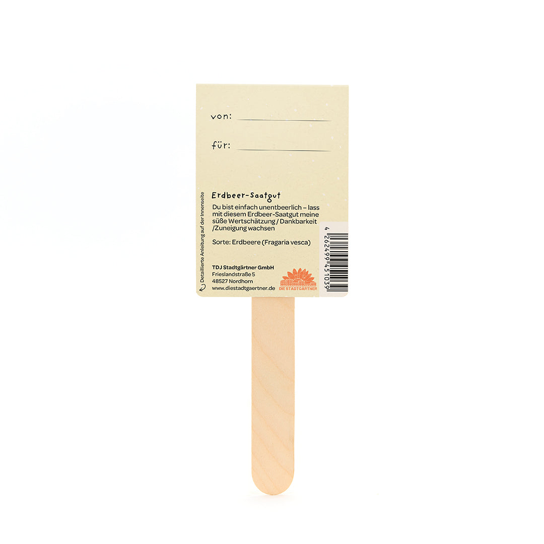 Parte posterior de una etiqueta de semillas de fresa en un palo de madera, con campos para "de" y "para" y una descripción de la semilla en alemán.
