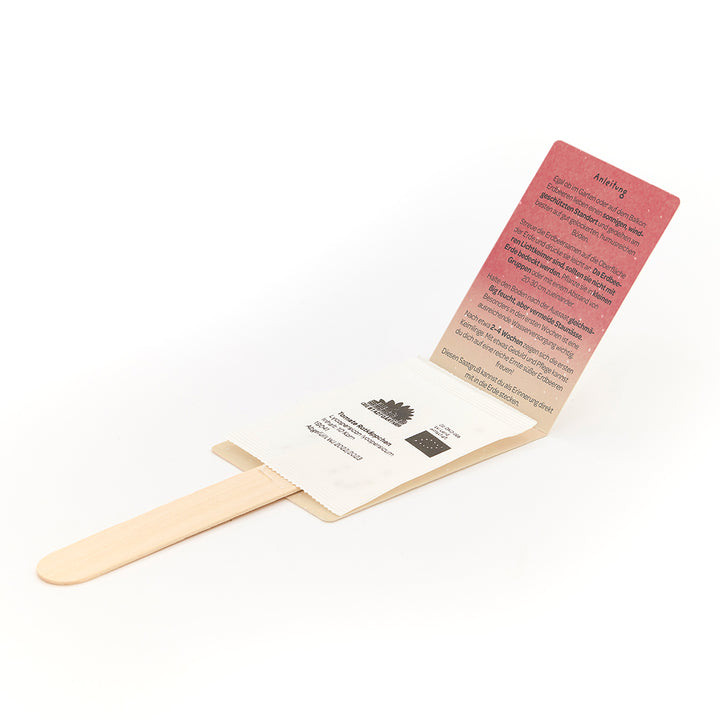 Un kit de semillas en forma de tallo de madera con embalaje de papel desplegado e instrucciones en alemán.