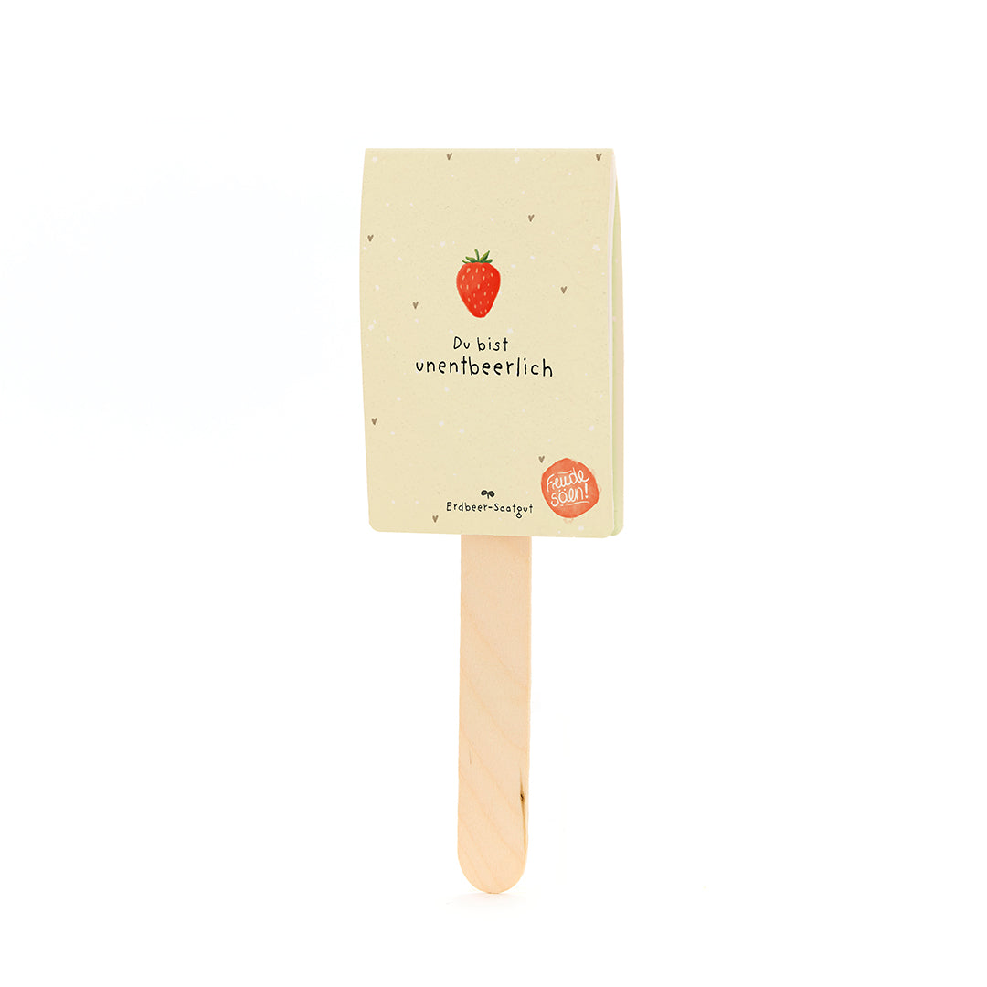 Palo de madera con una etiqueta que muestra una fresa y el texto "Eres indispensable" y "Semillas de fresa".