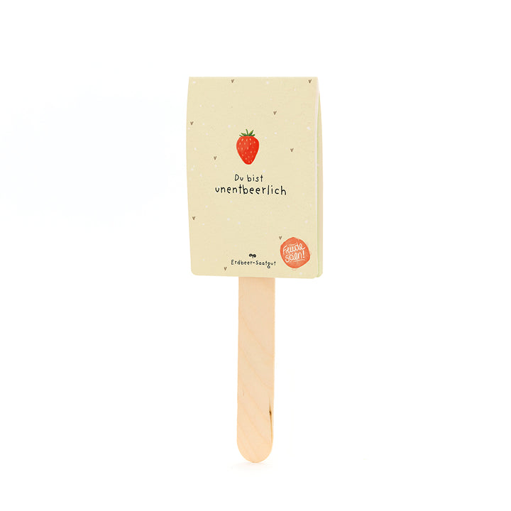 Palo de madera con una etiqueta que muestra una fresa y el texto "Eres indispensable" y "Semillas de fresa".