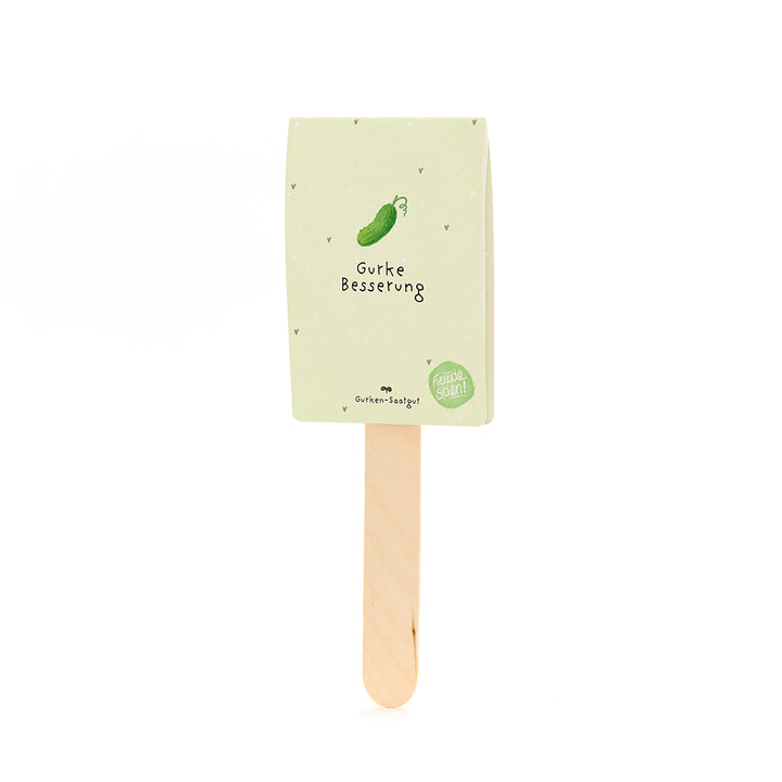 Un palo de madera con una etiqueta de papel de color verde beige que representa un pepino dibujado y el texto "Mejora del pepino".